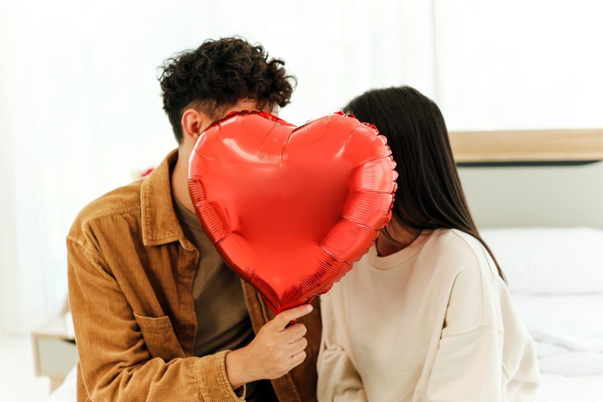 Szerelmes férfi egy szív mögé bújva súg valamit a párjának