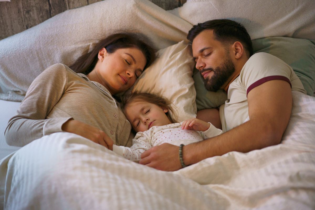 Egy család együttalvás közben: anyuka, kislány, apuka az ágyban.