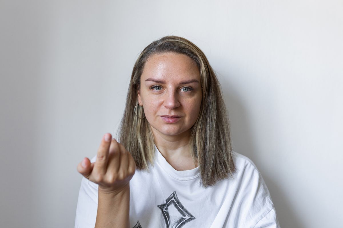 A confident woman with a warm expression extends her hand in an inviting gesture, set against a clean studio backdrop. This lifestyle portrait conveys friendliness, openness, and connection.