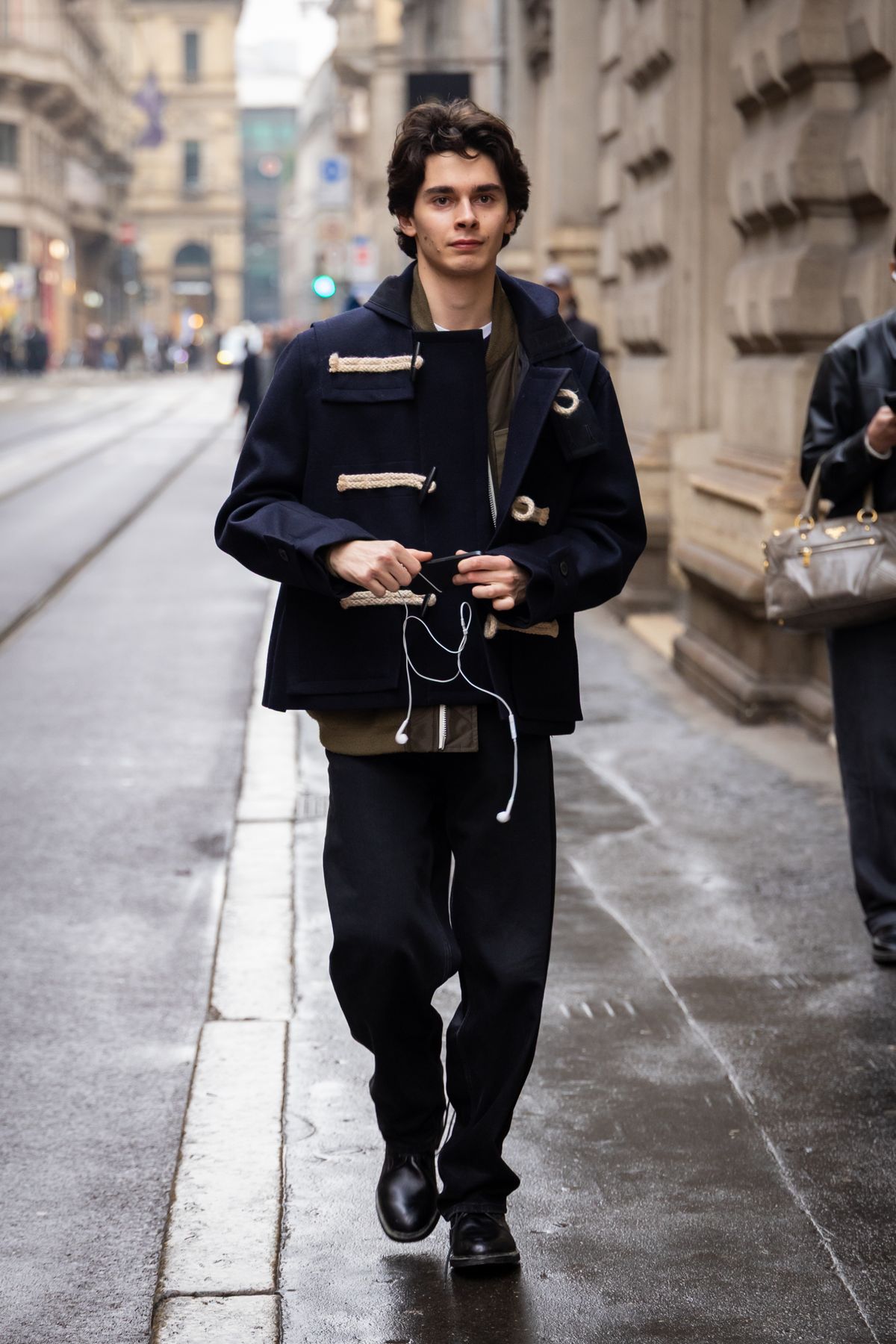 MILAN, ITALY - JANUARY 17: A guest wears a navy blue cropped duffle coat with white rope toggles, an olive green zip-up liner, a white t-shirt, dark navy wide-leg trousers, black leather boots, outside Lessico Familiare, during the Milan Fashion Week - Menswear Fall/Winter 2026-2027 on January 17, 2026 in Milan, Italy. (Photo by Claudio Lavenia/Getty Images)