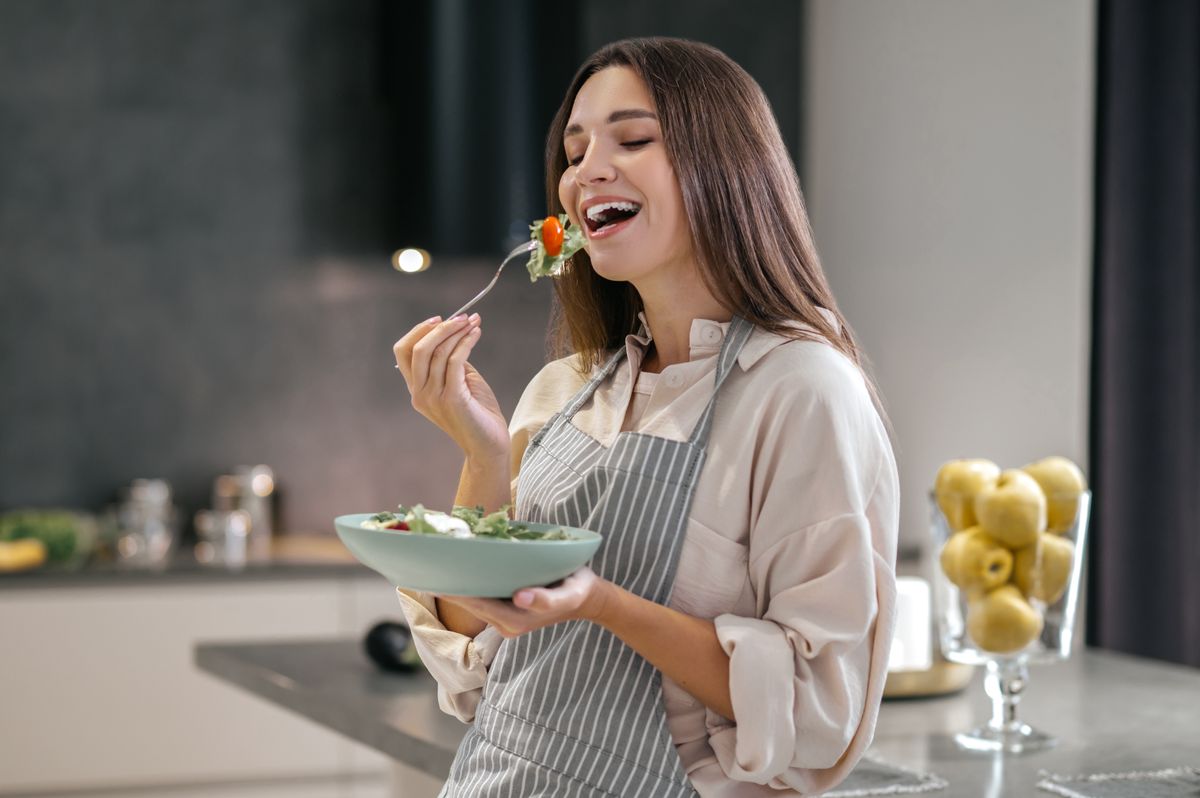 Salátát eszik a lány konyhában, méghozzá álva. Vajon a gyorsabb anyagcsere átok vagy áldás lesz az állva evés esetében?