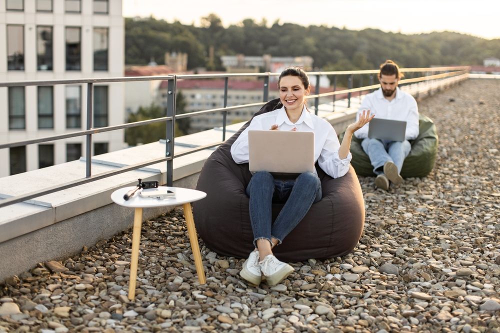 Fiatal nő és férfi babzsákon dolgoznak a teraszon, laptoppal: microshifting