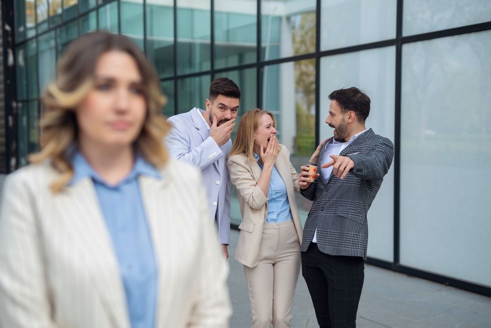 Nő háta mögött kollégák nevetgélnek, ha a munkahelyi románc véget ér.