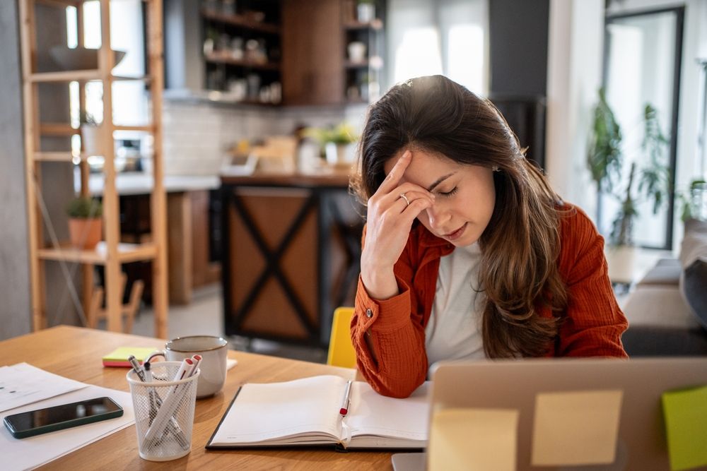 Fiatal kimerült nő home office-ban dolgozik - angyal segít lejjebb adni a maximalizmusát.