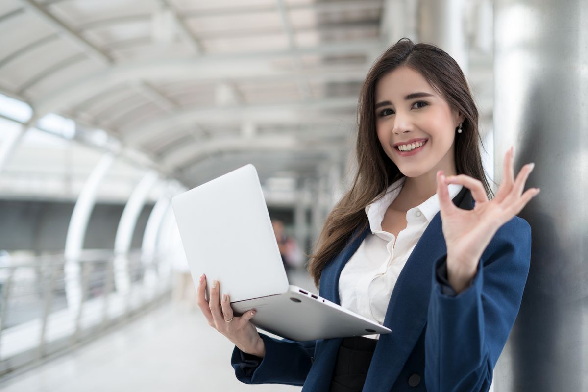 Business woman checking success work in laptop and show ok symbol. Toothy smiling business woman portrait