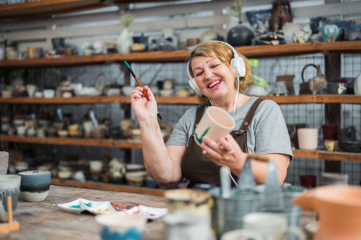 Egy boldog nő magas IQ-szinttel fest kerámiát fejhallgatóval a fején. 