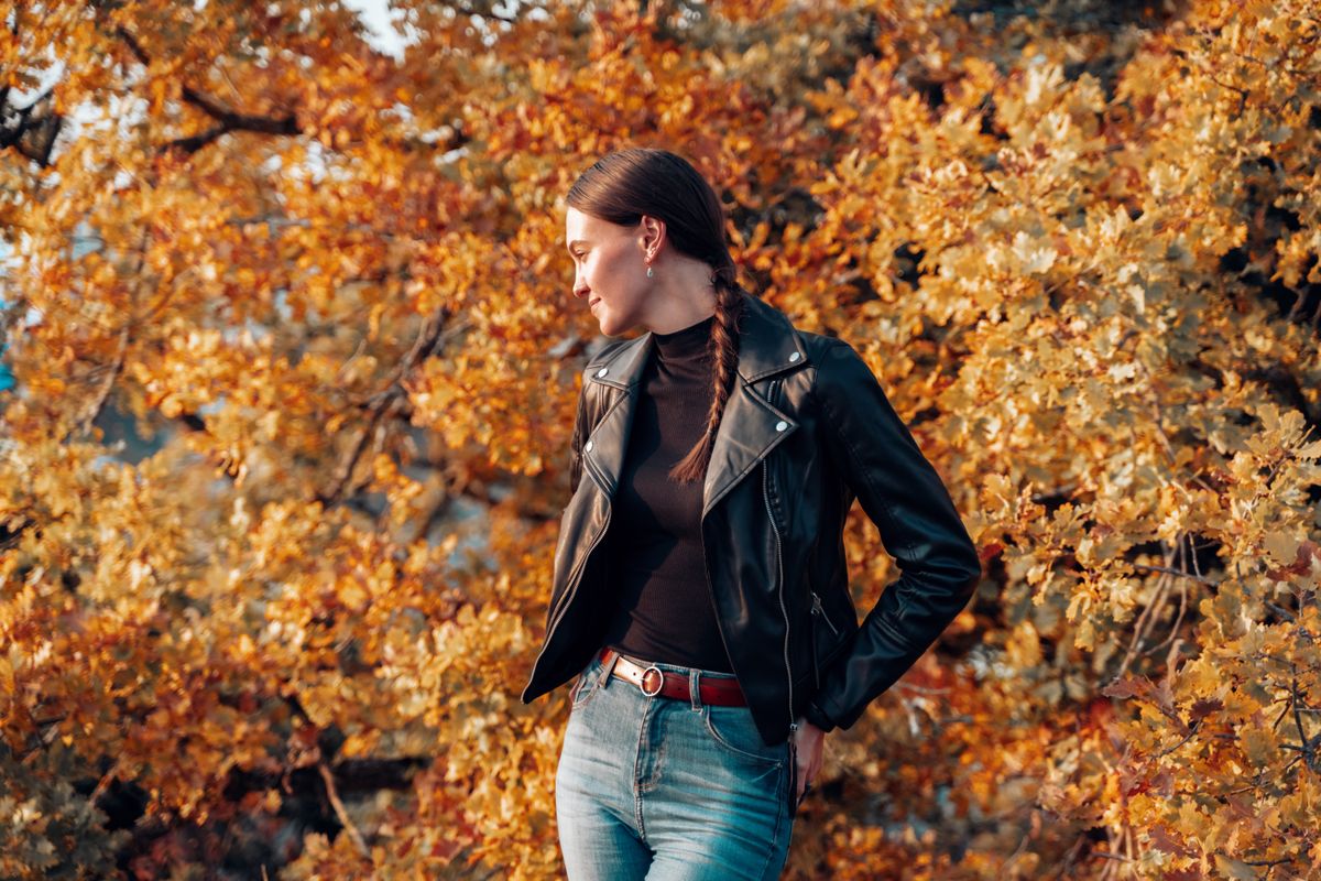 Young white European skinny woman enjoying Autumn forest and relaxing in the sun. She has braided hair and wears casual clothing