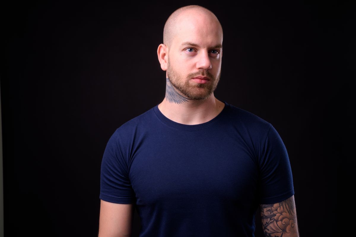 Studio shot of handsome bald bearded man against black background