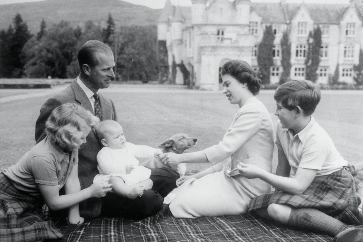 Baby Prince Andrew perches on Prince Philip's lap during a picnic on the grounds of Balmoral Castle. Looking on are Queen Elizabeth, Prince Charles, and Princess Anne.