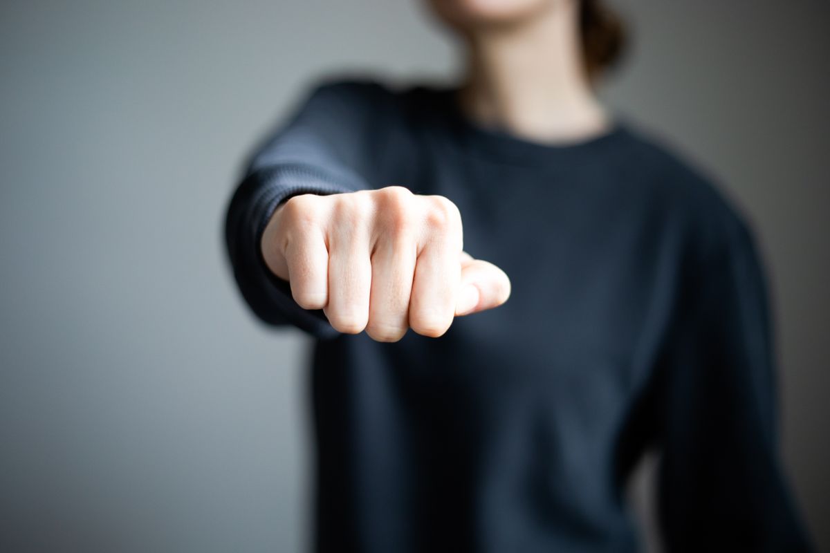 Személyiségteszt: egy nő ökölbe szorított kézzel fekete pulcsiban. 