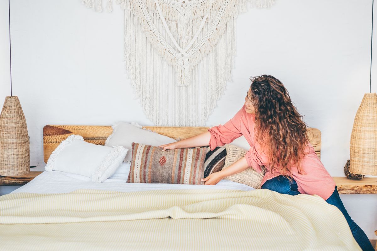 Egy nő az ágy bevetése közben rendezgeti a párnákat a hálószobában.