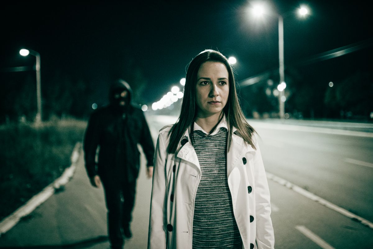 Otthon védelme: egy nő mögött egy betörő sétál a sötétben.