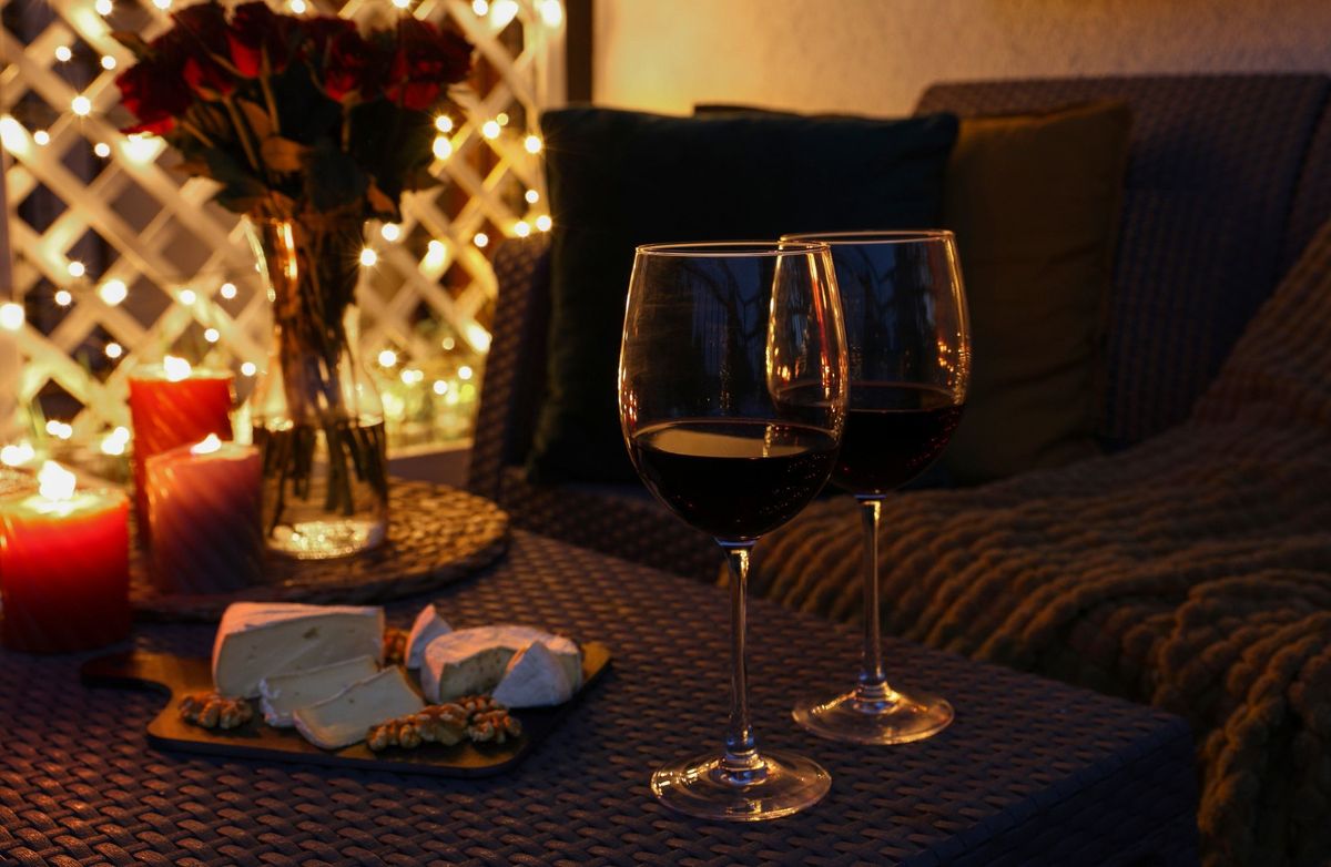 Glasses of wine, vase with roses, burning candles and snacks on outdoor terrace in evening