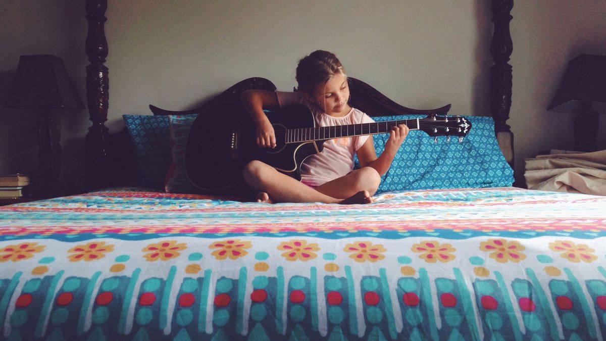 Gyereknevelés: egy kislány gitáron játszik az ágyon. 