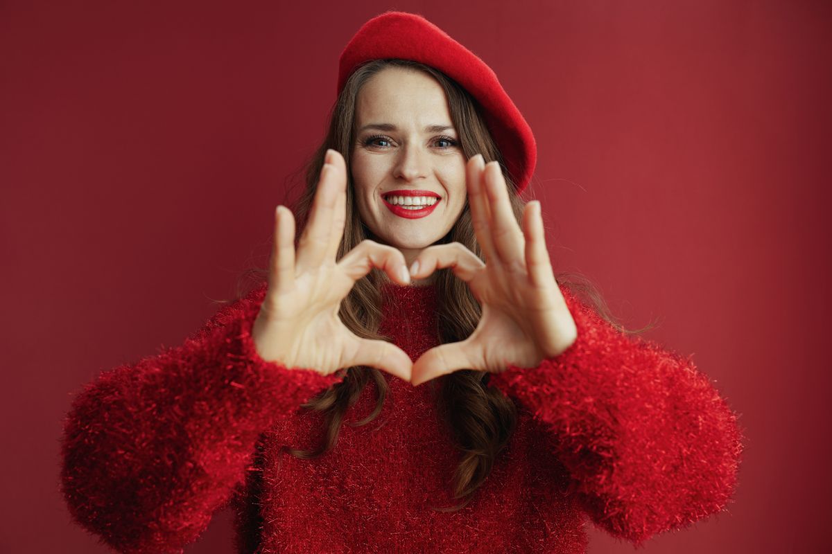 Valentin-napi divat egy pirosba öltözött fiatal nő szívet mutat a kamerának