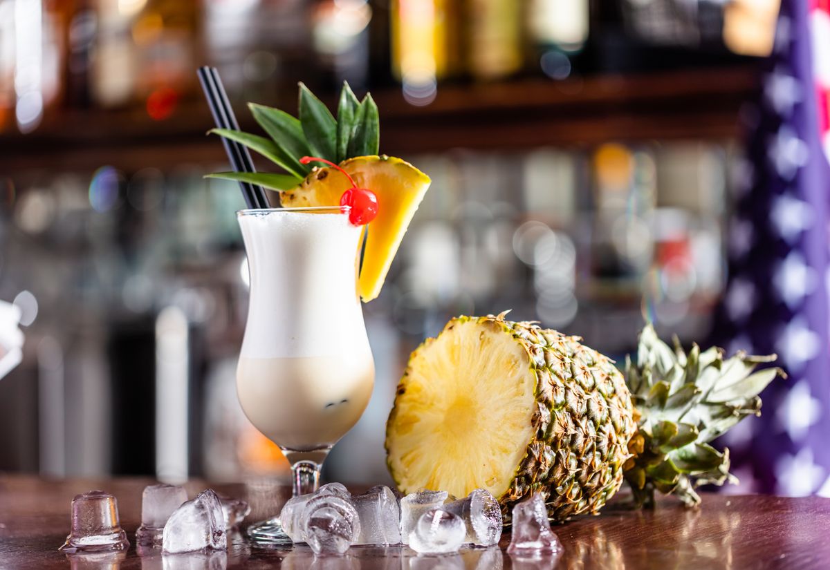 Pina colada coctail on bar counter with fresh pinapple and alcohol bottles.