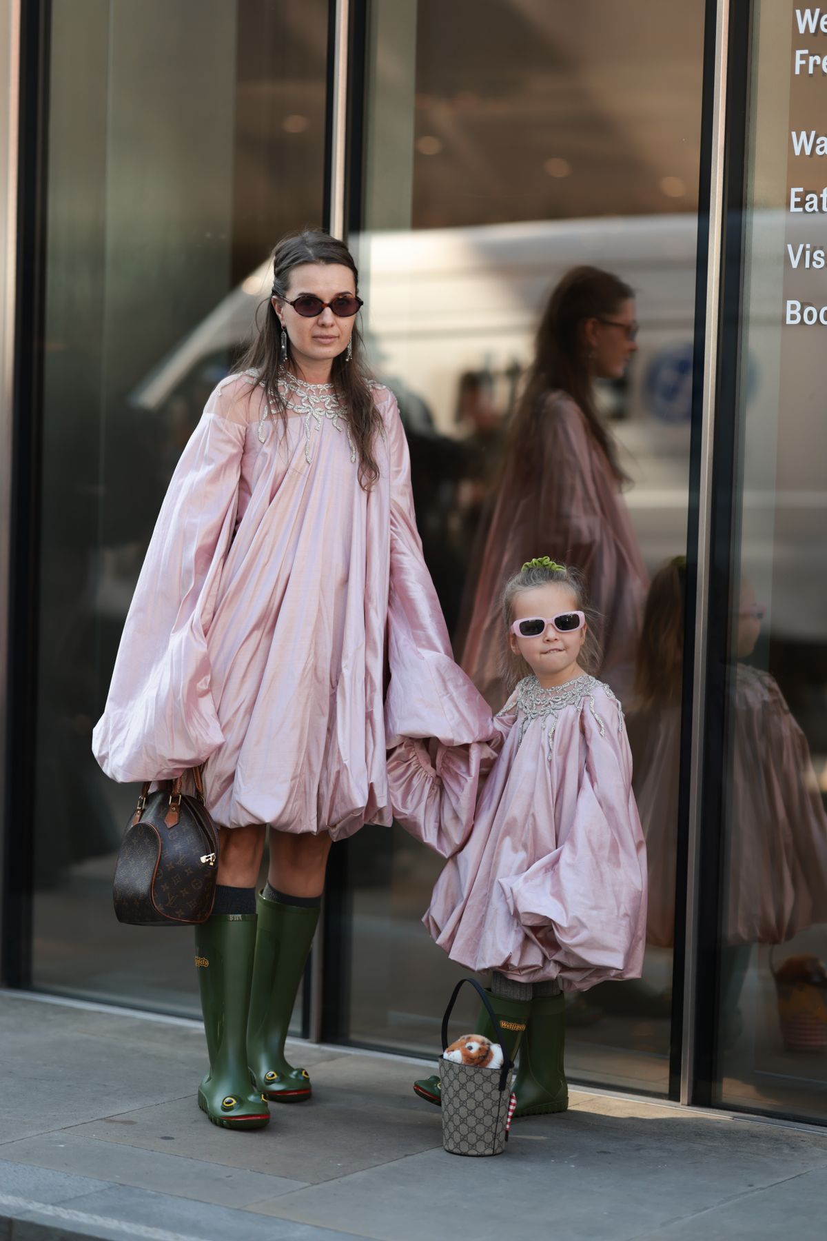 LONDON, ENGLAND - SEPTEMBER 19: A brown-haired Guest is seen wearing a rose puffer dress, green rubber boots with frog face and a Louis Vuitton leather handbag, sunglasses and silver earrings and her daughter seen wearing the matchy outfit, rose puffer dress, green rubber boots with frog face, rose sunglasses, a green hairband and a Gucci bag with stuffed animal outside MITHRIDATE Show during London Fashion Week on September 19, 2025 in London, England. (Photo by Jeremy Moeller/Getty Images)