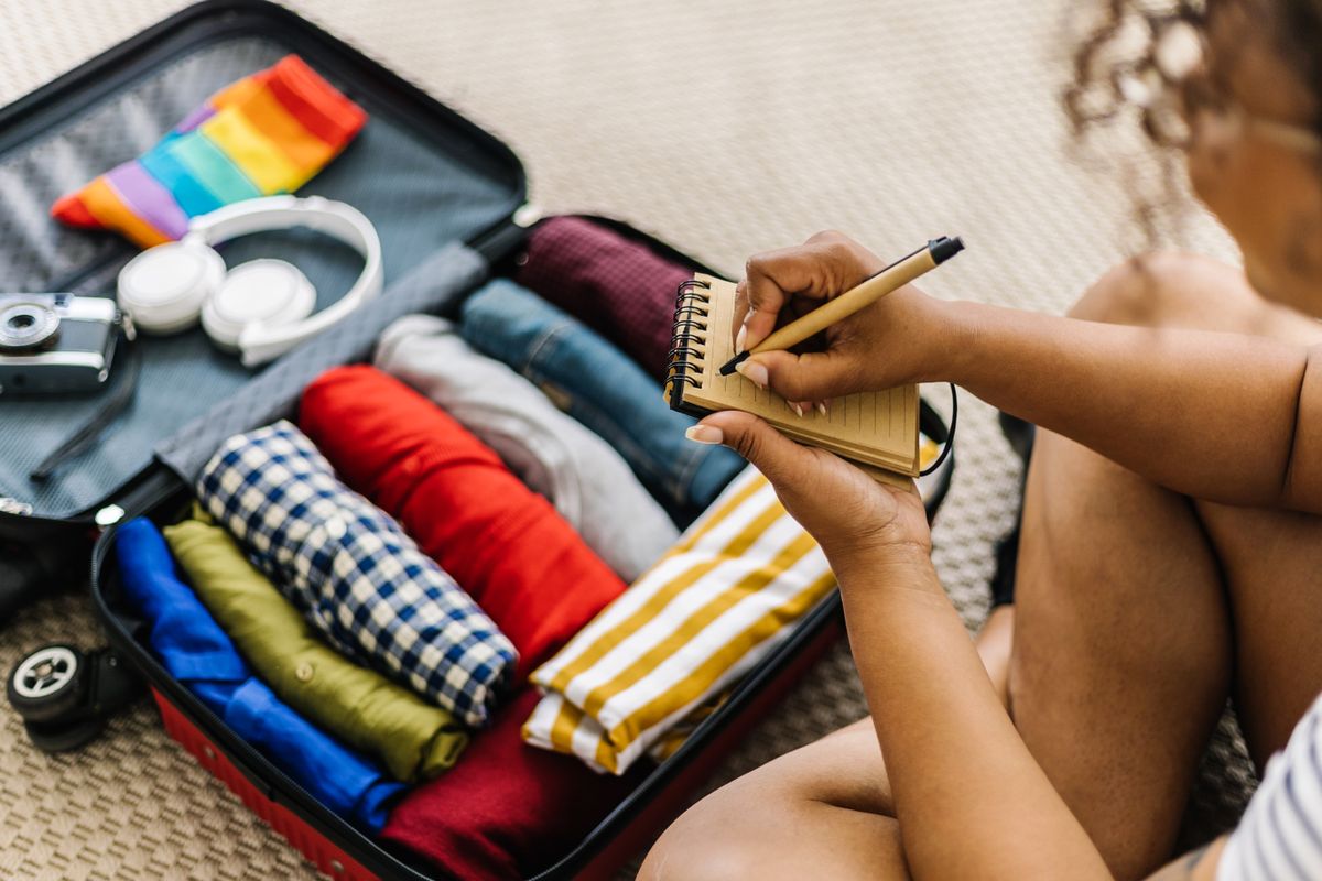 Mixed race young adult woman writing list of accessories and travel stuff before going on summer holidays - Travel and vacation concept