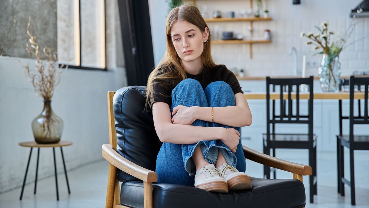 beteljesületlen szerelem, egy fiatal nő szomorúan ül egy fotelban, lábait átkulcsolva