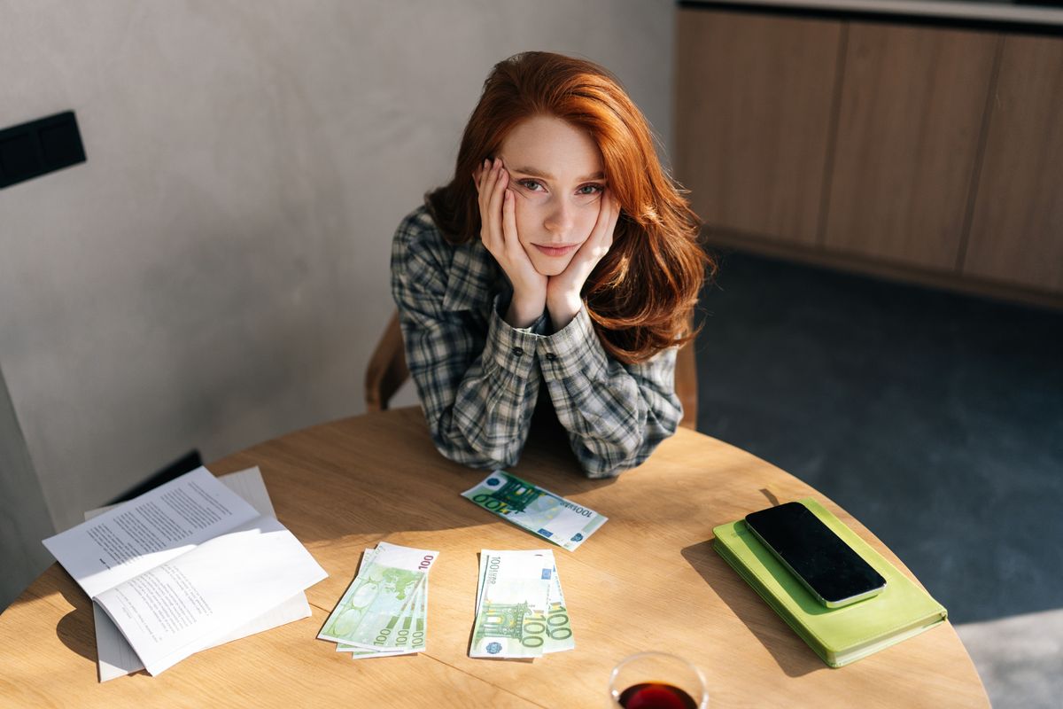 pénzt számoló, szegénységben felnőtt vörös hajú nő az asztalnál