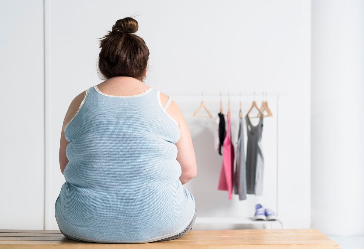 Teenaged overweight girl sitting at a bench near a clothing rack.