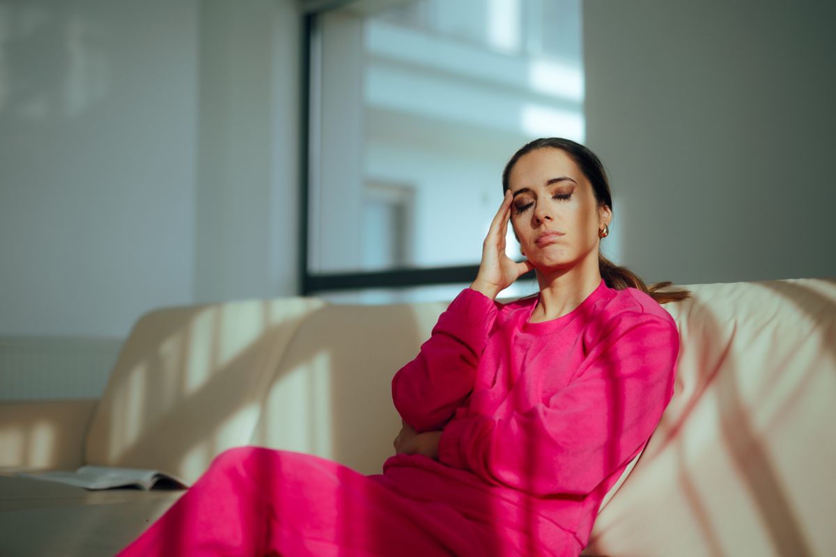 Perimenopauza, egy középkorú nő rózsaszín ruhában gondterhelten ül a kanapén. 