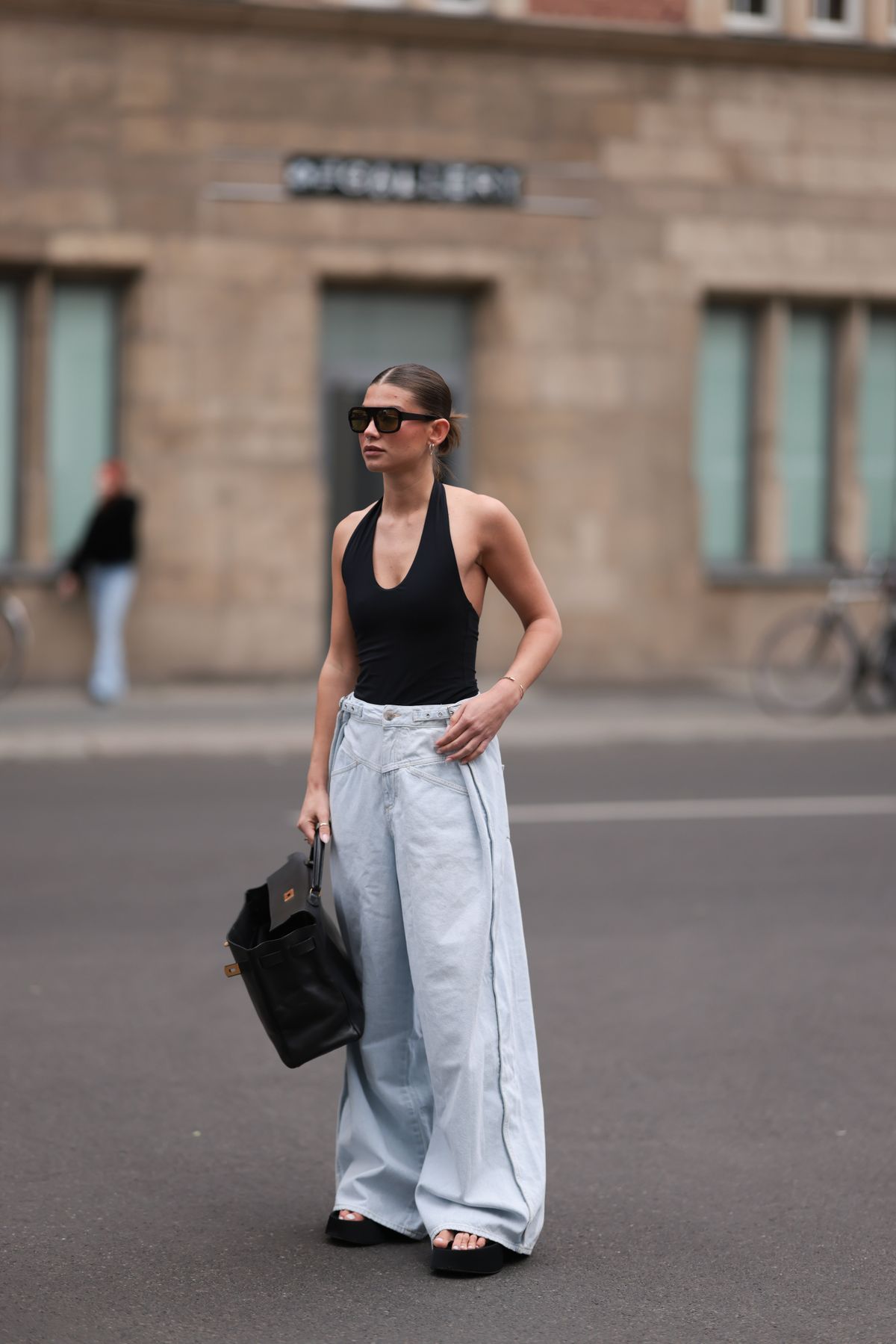 BERLIN, GERMANY - MAY 22: Sophia Geiss is seen wearing silver hoop earrings in two different sizes, large aviator sunglasses with a bold black frame and green lenses from Vehla Eyewear, a silver nose ring, a black halter-neck bodysuit with a round neckline from Mango, high-waisted wide-leg pleated jeans in a light wash with a double waistband from Closed, a rectangular black leather "Kelly 40" bag from Hermès, a gold bangle, a silver ring, and black platform flip-flops from Zara on May 22, 2025 in Berlin, Germany. (Photo by Jeremy Moeller/Getty Images)