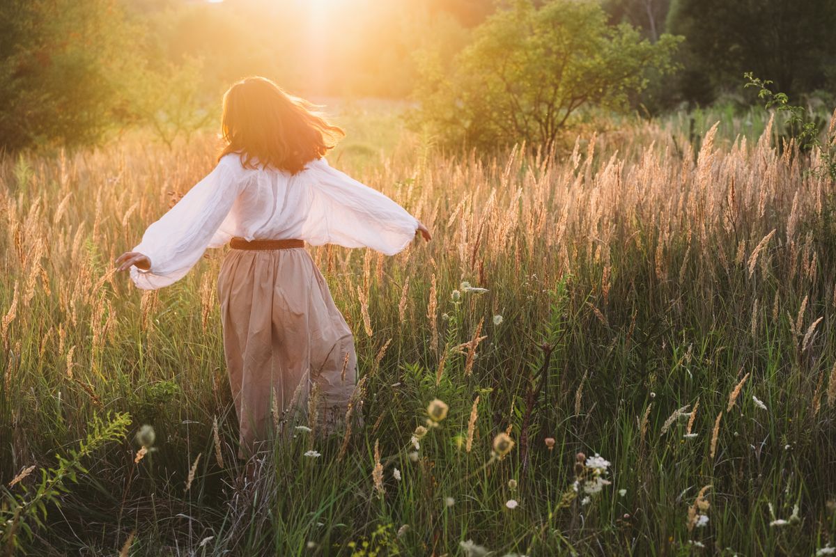 csillagjegyek, egy fiatal nő a napfényben sütkérezik egy búzamezőn.