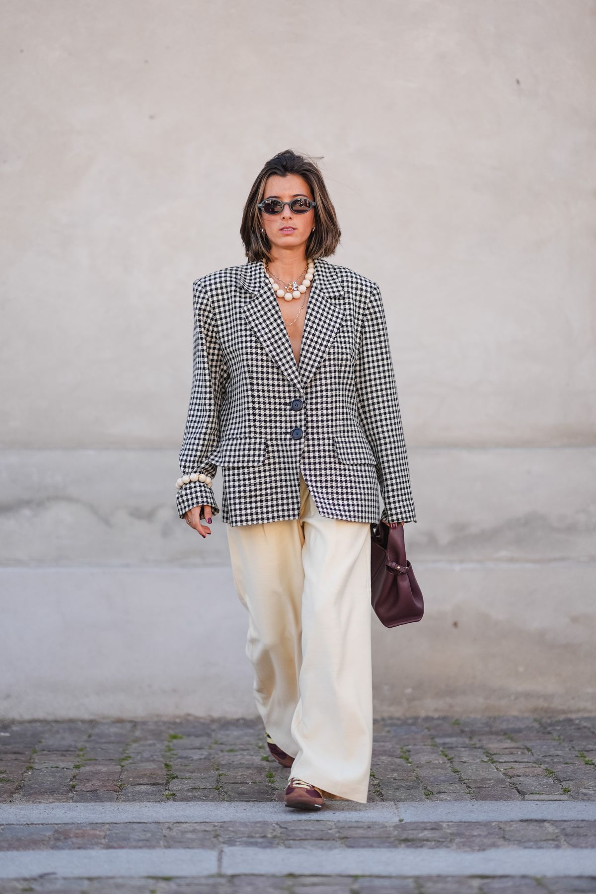 COPENHAGEN, DENMARK - AUGUST 6: A guest wears black sunglasses, silver necklace, white beaded necklace, black and white pattern oversized blazer jacket, silver rings, white pearl beaded bracelet,cream flowy pants, shiny dark brown leather bag, light brown shoes, outside Lovechild 1979, during the Copenhagen Fashion Week Spring/Summer 2024-2025 on August 6, 2024 in Copenhagen, Denmark. (Photo by Edward Berthelot/Getty Images)