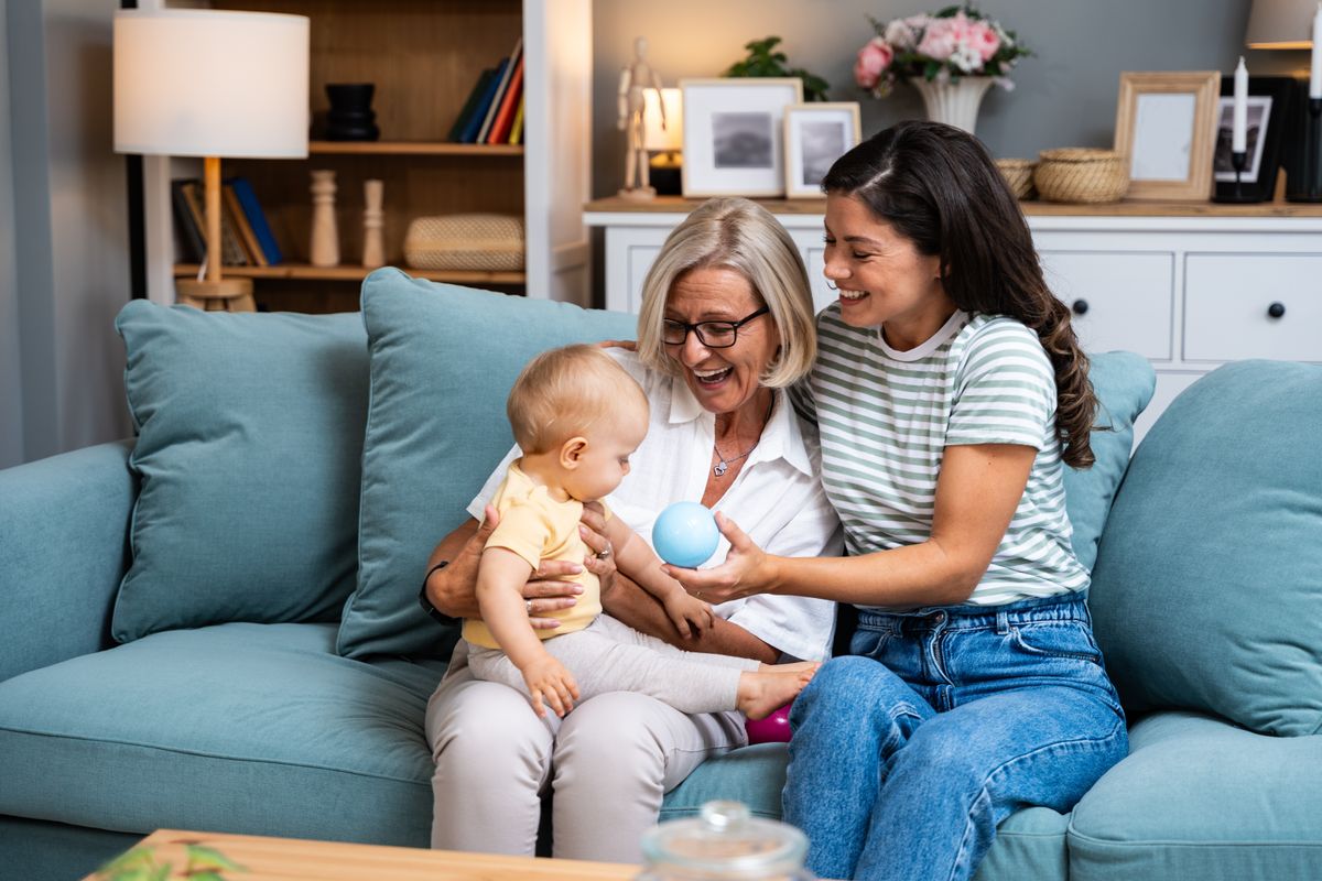 gyereknevelésben résztvevő nagyszülő, ölében az unokával, mellett a lánya ül