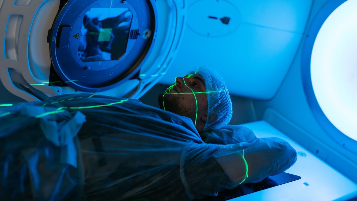 Rákkutatások egyik modernebb módszereként  egy férfi fekszik radioterápia közben egy gépben, aminek köszönhetően sugárzással pusztítják a daganatos sejteket. 