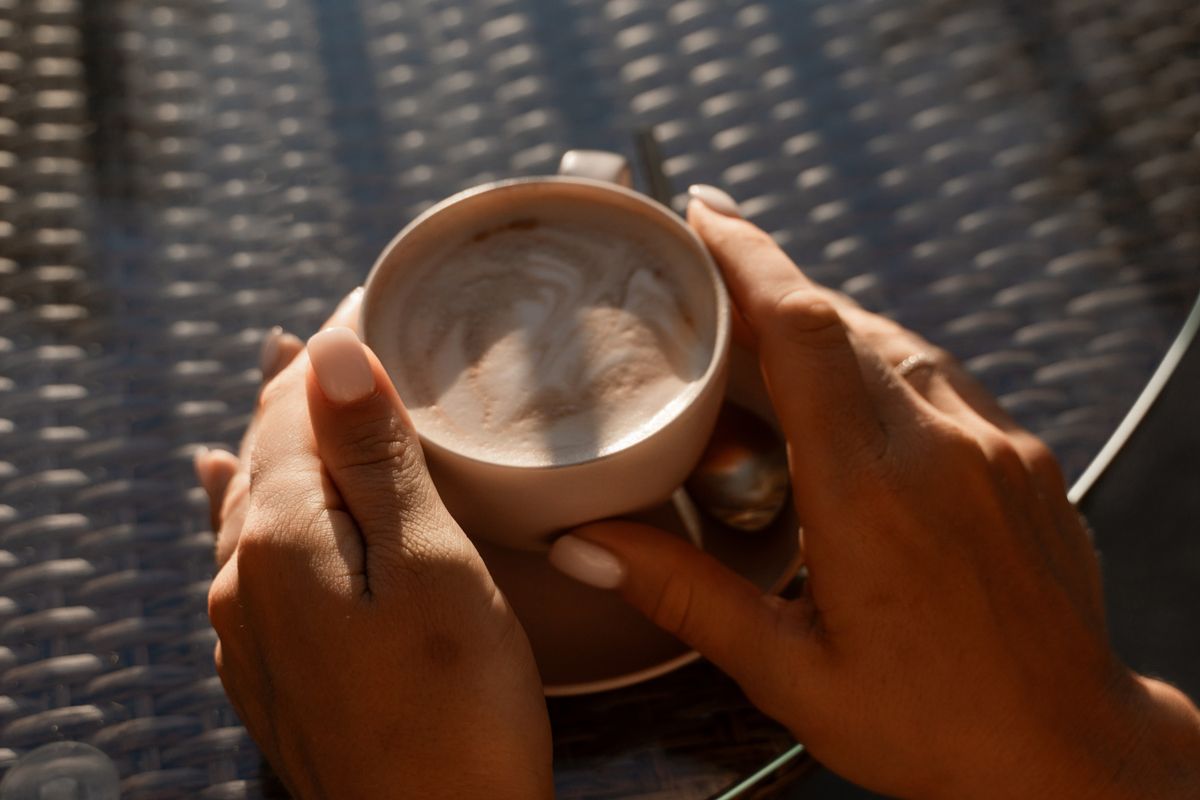 Coffee Hands Cup - Close-up of a woman's hands holding a cup of coffee with latte art, shot from above.
