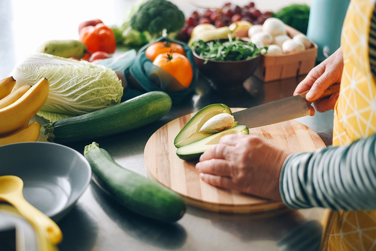 A woman cuts a ripe avocado and takes out a stone from it on a wooden plank. Fresh vegetables. Salad preparation. Diet food. Ecological products.