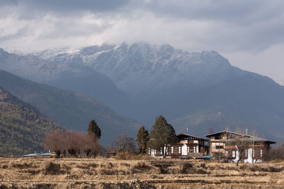 Farmhouses in the Paro Valley with a snow-capped mountain shrouded with clouds in the background. (Photo by: Jon G. Fuller/VW Pics /Universal Images Group via Getty Images)