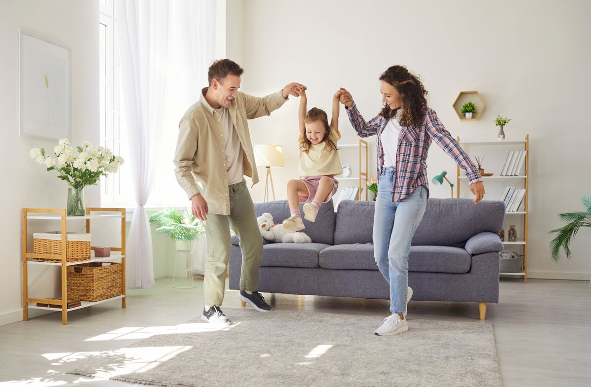 Family parents support daughter play at home. In livingroom, the child girl laughs with mother and father by sofa, sharing fun, love, and support. Happy family bonding and playful trust.