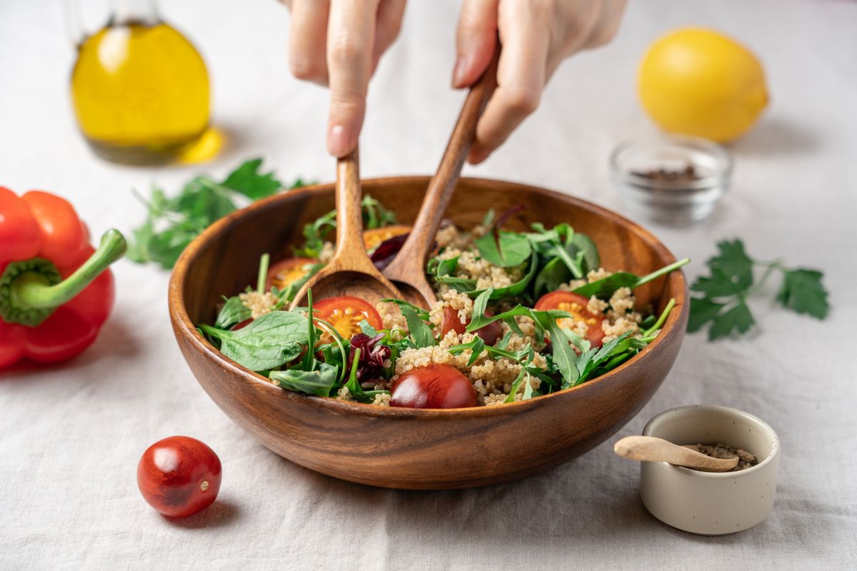 Female Hands Mixing Quinoa Salad with Cherry Tomatoes and Fresh Greens in Wooden Bowl Using Wooden Spoons. Healthy Diet Food Concept