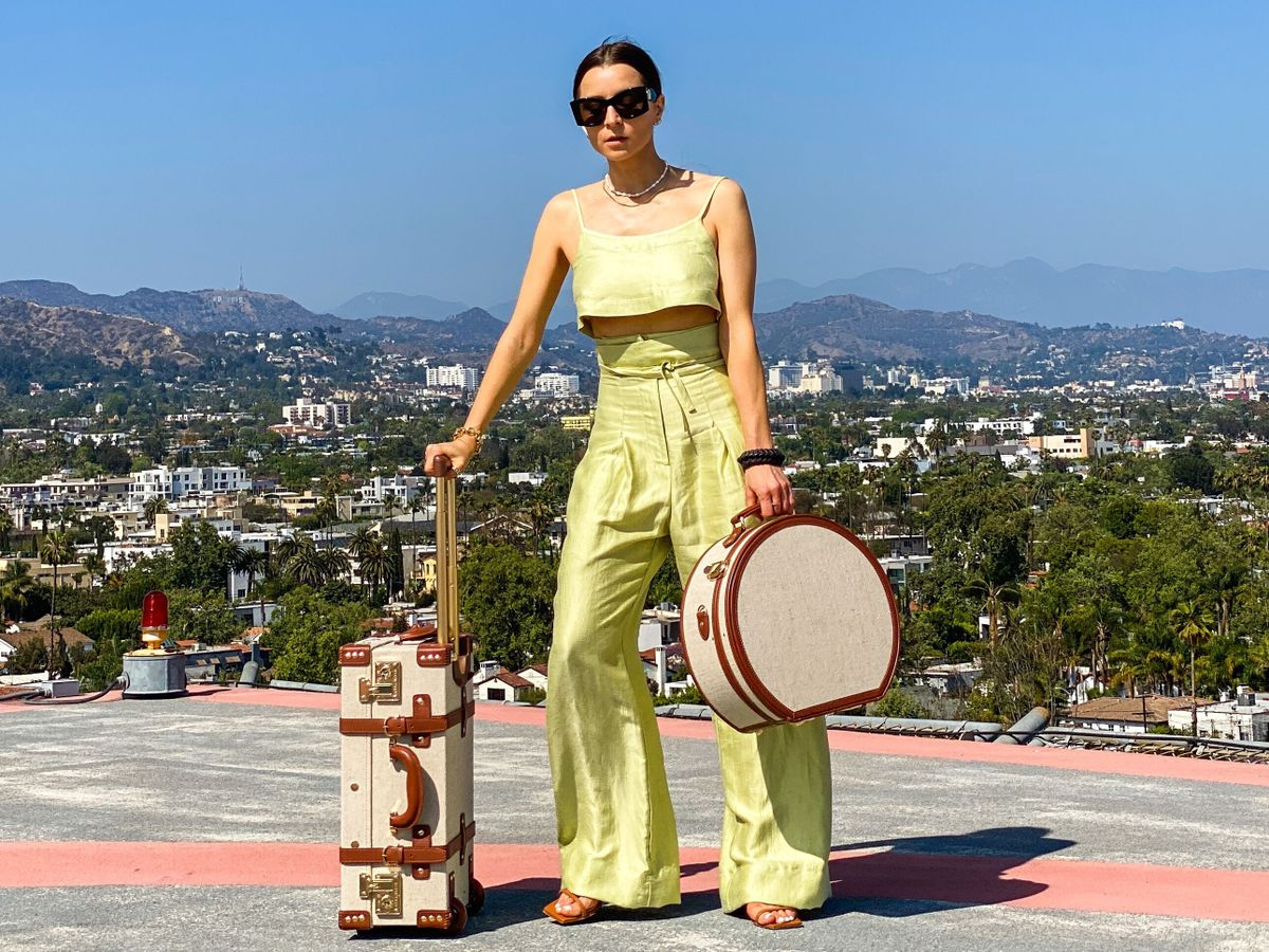 PARIS, FRANCE - MAY 13: Julia Comil wears a lime sorbet cropped linen cami top by Bondi Born, lime sorbet high waisted linen pants by Bondi Born, sandals by wandler, sunglasses by Lanvin, vintage hat box by Steamline luggage, vintage linen and leather cabin luggage by Steamline luggage, during an online remote street style fashion photo session via Apple iphone / Facetime and the CLOS app as the model is located in Beverly Hills - California and the photographer in Paris - France, on May 13, 2021 in Paris, France. (Photo by Edward Berthelot/Getty Images)