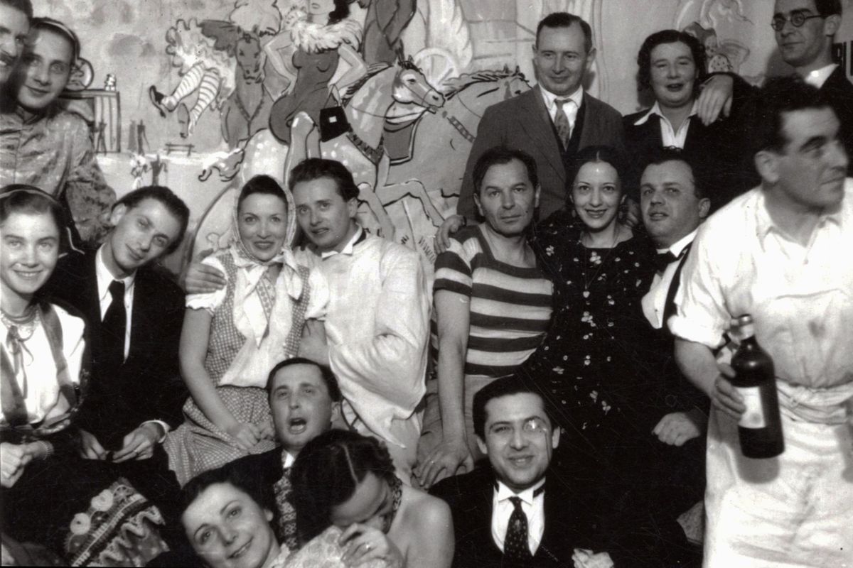 Gül Baba utca 36., házavató Péter Andráséknál 1938. január 15-én. Bal oldalon Kolozsvári Grandpierre Emil író, előtte Gyarmati Fanni és Radnóti Miklós, mellettük Péter Andrásné és Ortutay Gyula néprajzkutató. Előrébb Halász Gábor író és monoklival Joó Tibor irodalomtörténész. Jobb oldalon fehér köténnyel Péter András művészettörténész (házigazda), mellette Hevesi András író, fölötte Reitzer Béla szociológus.