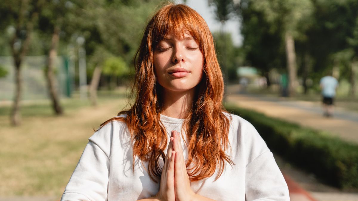Young redhead caucasian woman student teenager girl meditating warming-up before training, feeling zen-like while jogging running outdoors in park. Active lifestyle concept.