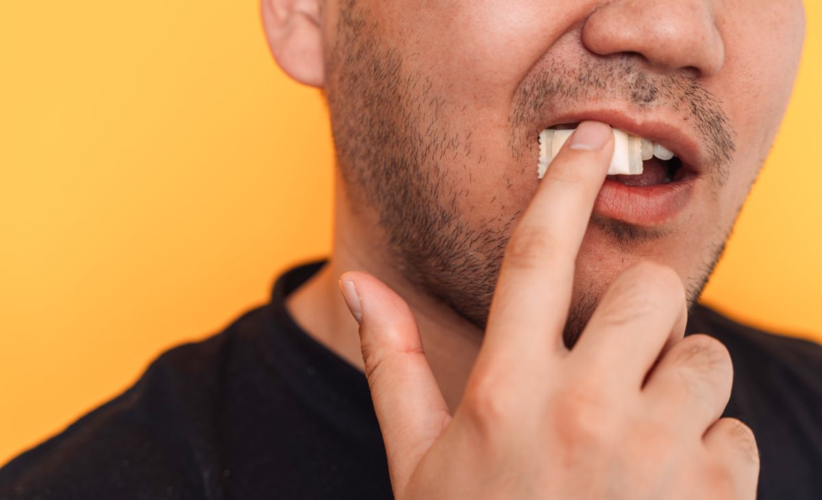 A man puts a non-smoking tobacco product under his lip against a yellow background.