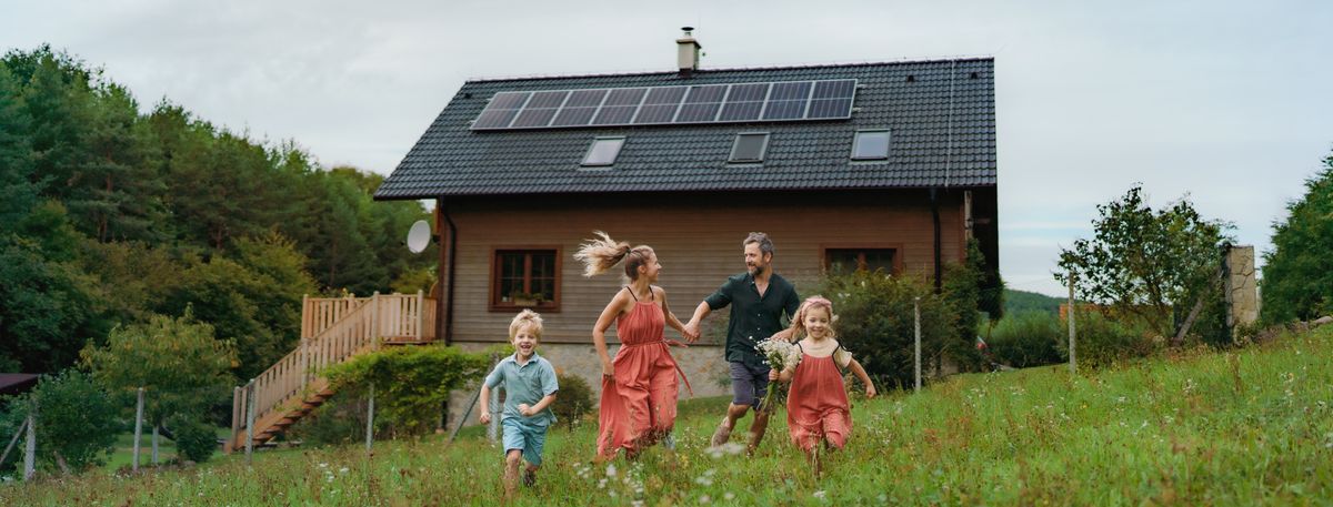 Happy family running near their house with solar panels. Alternative energy, saving resources and sustainable lifestyle concept.