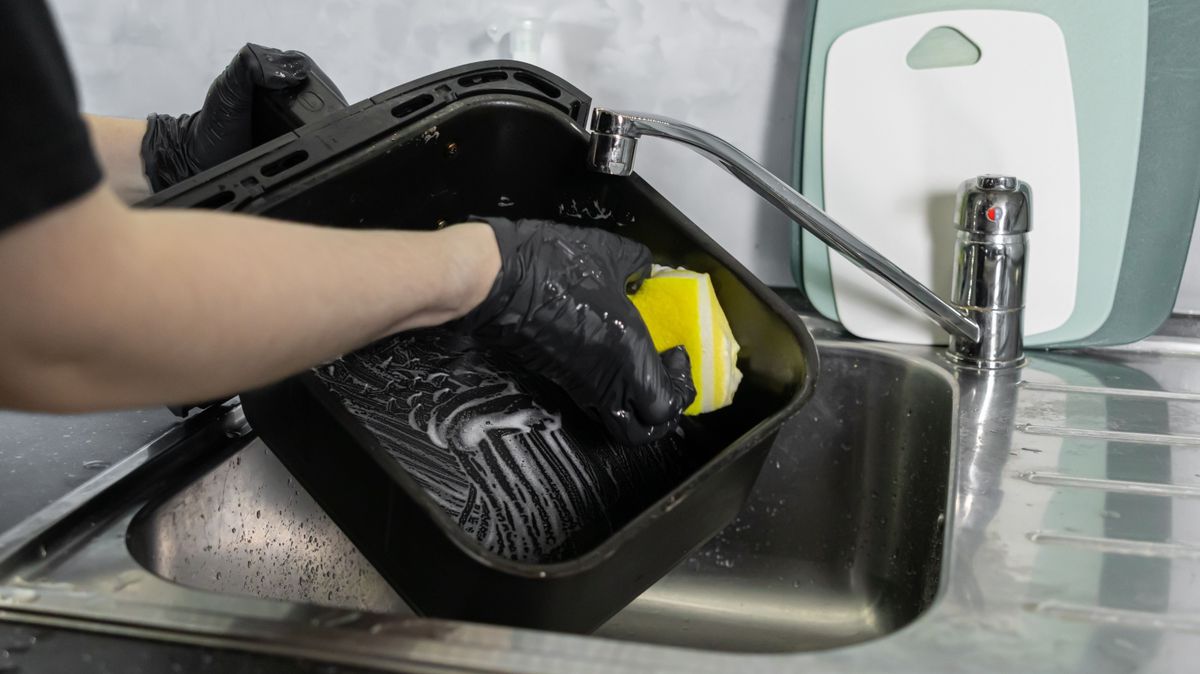 Az airfryer kosarát tisztítja egy nő mosogatószivacs segítségével.