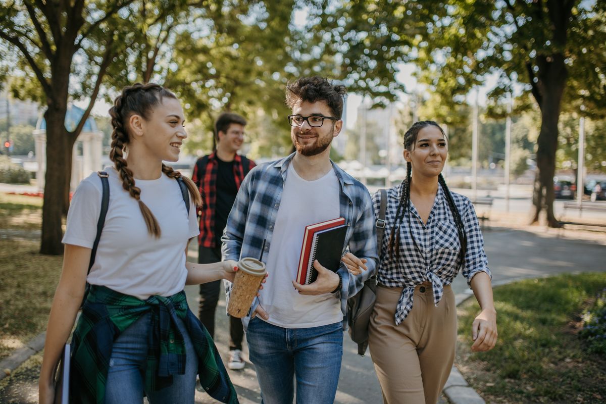 Group of cheerful male and female students chatting and smiling while walking in University campus