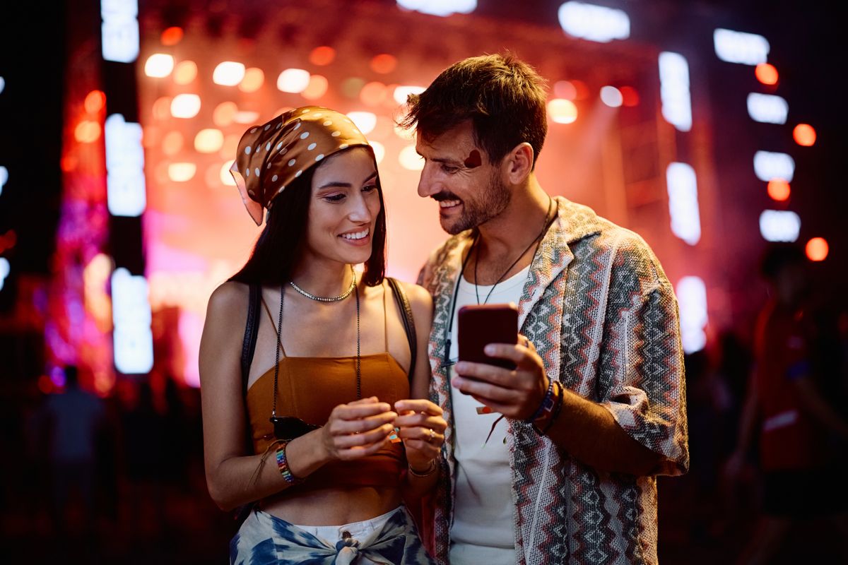 Happy festival goers using app on smart phone on summer music concert at night.