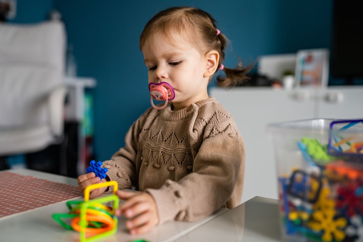 One child small caucasian girl little toddler with nipple pacifier playing at the table at home alone childhood growing up concept copy space