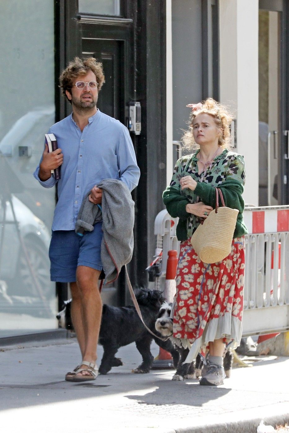 *EXCLUSIVE* London, UNITED KINGDOM Helena Bonham Carter, 58, is spotted linking arms with her boyfriend Rye Dag Holmboe, 36, as they enjoy a dog walk together. Bonham Carter shows off her distinctive sense of style in a green patterned cardigan layered over a floral top, paired with a red floral midi skirt featuring a contrasting light-coloured hem. She completes the look with grey socks and grey lace-up trainers, while carrying a woven straw shoulder bag and wearing sunglasses. Holmboe is seen wearing a light blue button-up shirt with blue shorts and sandals, carrying books under one arm and holding a grey jumper in the other as he walks their dogs. Bonham Carter is also seen wearing a ring on the ring finger of her left hand as the couple stroll together, sparking rumours about a possible engagement. *Pictures Containing Children Please Pixelate Face Prior To Publication*,Image: 1128557361, License: Rights-managed, Restrictions: RIGHTS: WORLDWIDE EXCEPT IN UNITED KINGDOM, Model Release: no , Pictured: Helena Bonham Carter, Rye Dag Holmboe