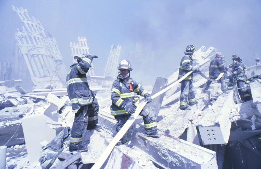 A New York-i Tűzoltóság tűzoltói tömlőt húznak, hogy eloltsák a kisebb tüzeket a Marriott Hotel romjai között és a második, összeomlott toronyban a World Trade Center elleni 9/11-es támadás után.