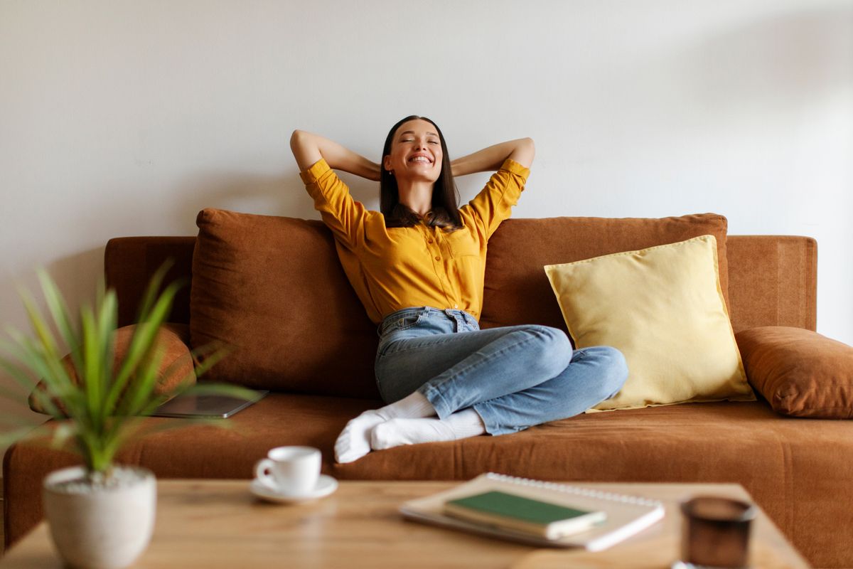 Peaceful woman sitting with her hands behind her head on comfortable couch, embodying relaxation and ease, free space