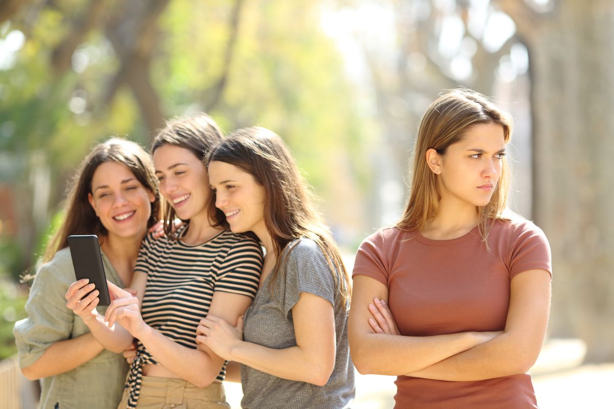 Angry woman being ignored by her happy friends who are checking smart phone content in the street