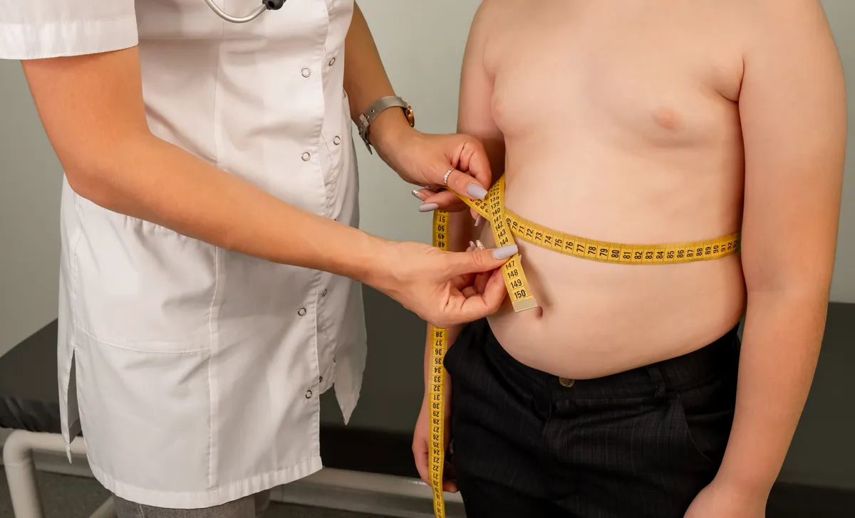 Concept of excessive weight, obese, dieting, overweight. Childhood obesity problem and weight loss. Doctor examining fat boy in clinic. Fat boy at a nutritionist appointment. Flabby skin on fat belly.